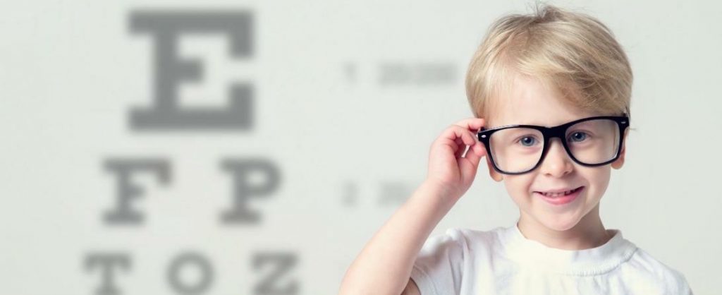 A young boy with glasses focuses on an eye chart during a routine eye exam.