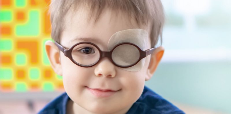 A young boy with glasses and an eye patch, looking determined and confident.