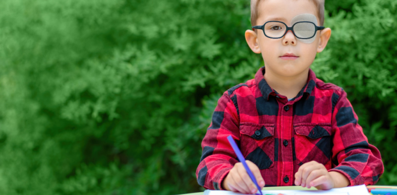A young boy with glasses and a red shirt is drawing, highlighting the exploration of children's vision problems