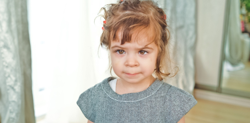 A young girl with a sorrowful expression standing before a mirror, reflecting her sadness