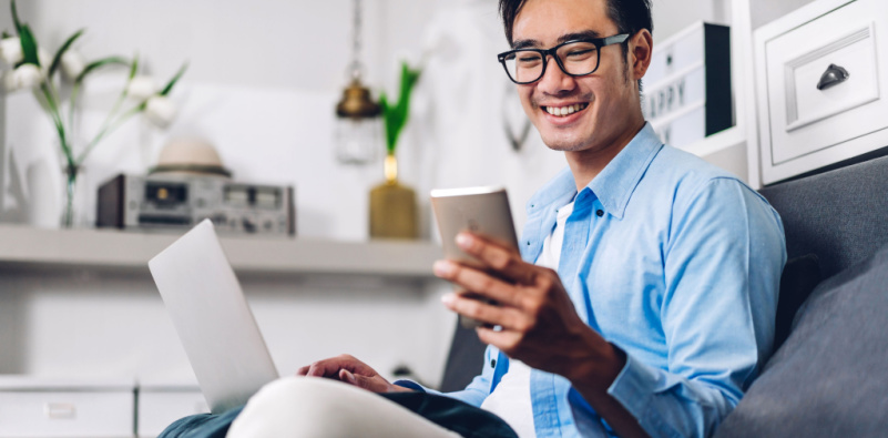 A man wearing glasses is sitting on a couch with a laptop in front of him