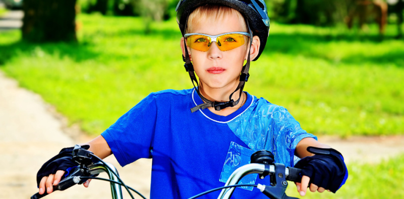 A child riding a bicycle wearing helment and glasses