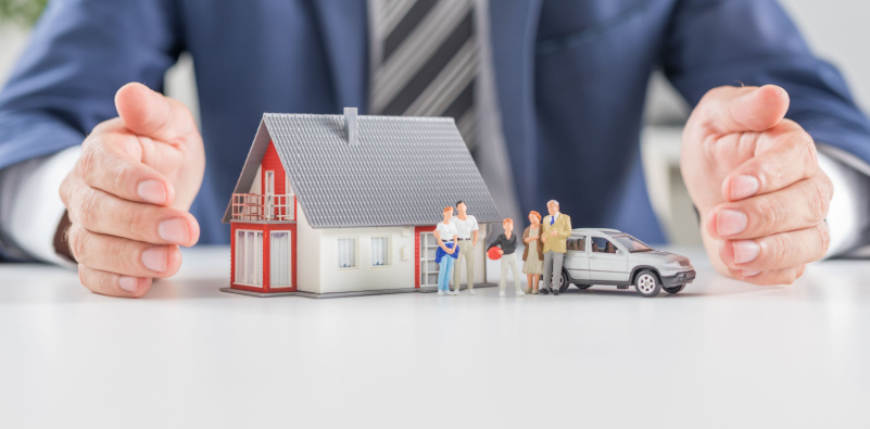 A man in a suit displays a miniature house and car