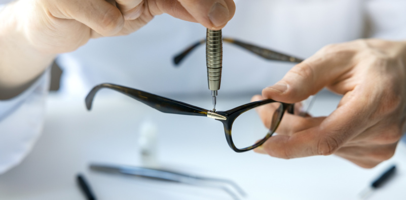 A person holding glasses and tools in his hands for repairs or adjustments.