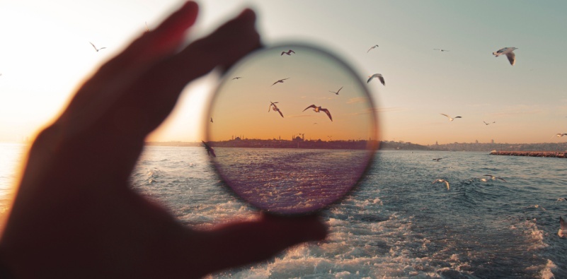 A hand holding up a polarized sunglass lens to the sea