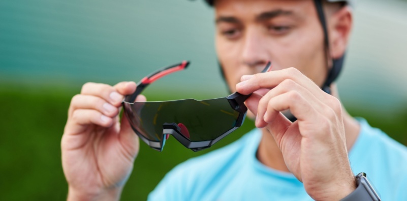 A man holding a pair of sport sunglasses in front of his face
