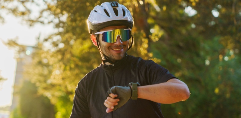 A cyclist wearing sporting sunglasses, smiling and looking at his watch