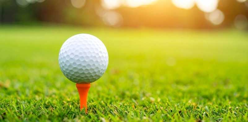 A close-up of a golf ball on a tee with sun glare in the background